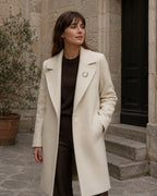 Laurea gold-finish freshwater pearl wreath brooch worn on the lapel of an ivory coat.
