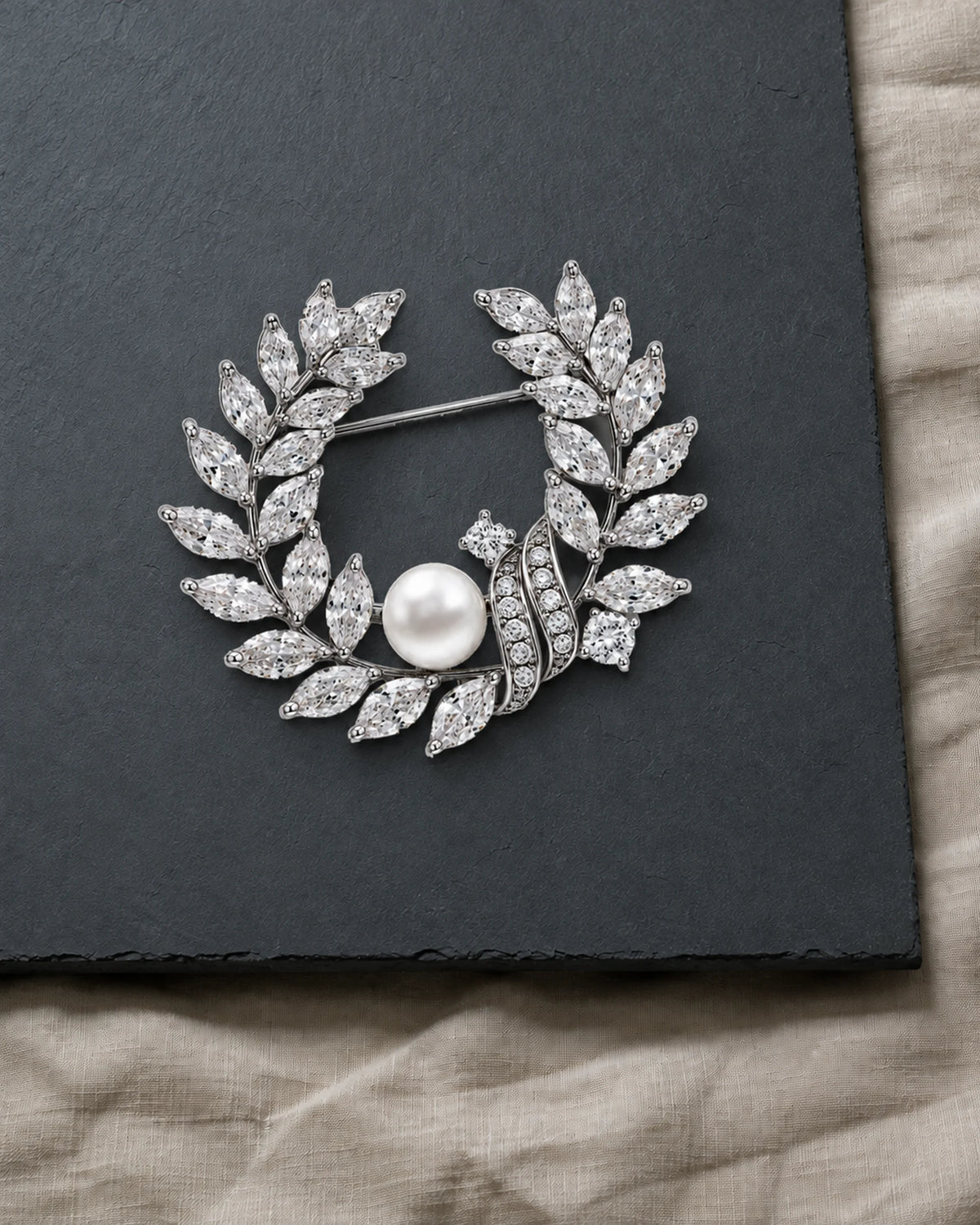 Laurea silver freshwater pearl leaf wreath brooch resting on a charcoal slate surface.