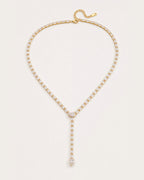 Liora Gold Crystal Y-Drop Necklace resting on a soft #F0EBE9 studio surface