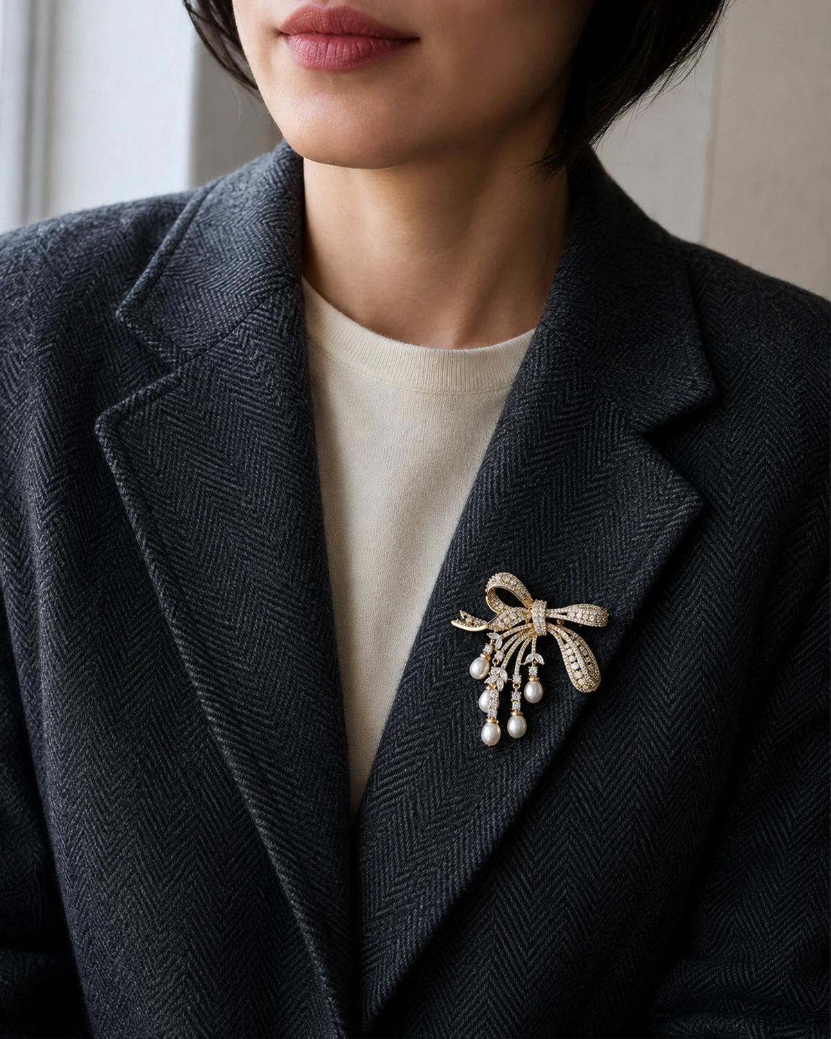 Lova Freshwater Pearl Bow Brooch pinned within a charcoal herringbone blazer lapel