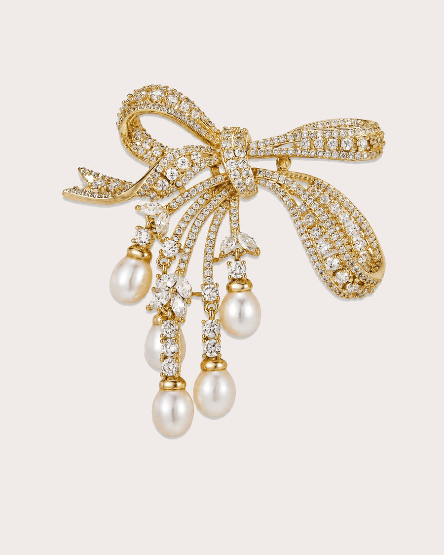 Gold-tone bow brooch with five freshwater pearl drops on a warm neutral background