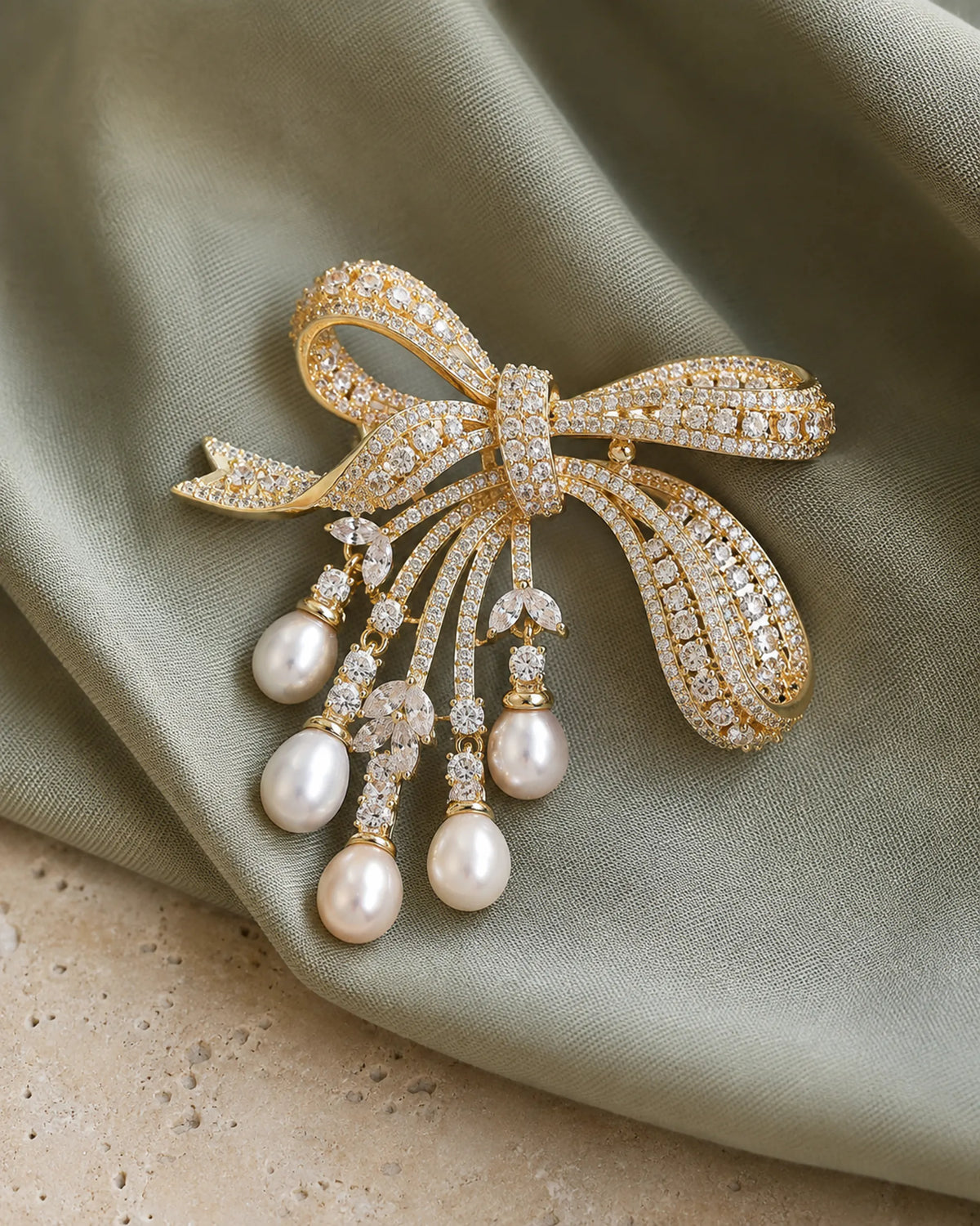 Gold ribbon bow and five freshwater pearl drops resting on muted sage fabric