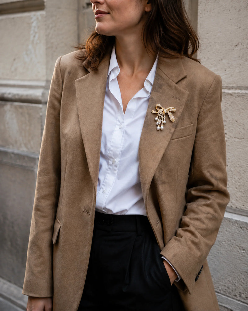 Gold-tone freshwater pearl bow brooch styled on a camel blazer with a white shirt