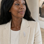 Woman wearing the Lumi Crystal Feather Brooch at true 6.5 cm scale on an ivory blazer
