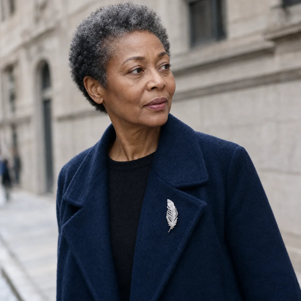 Black woman wearing the Lumi Crystal Feather Brooch at true 6.5 cm scale on a navy wool coat outdoors