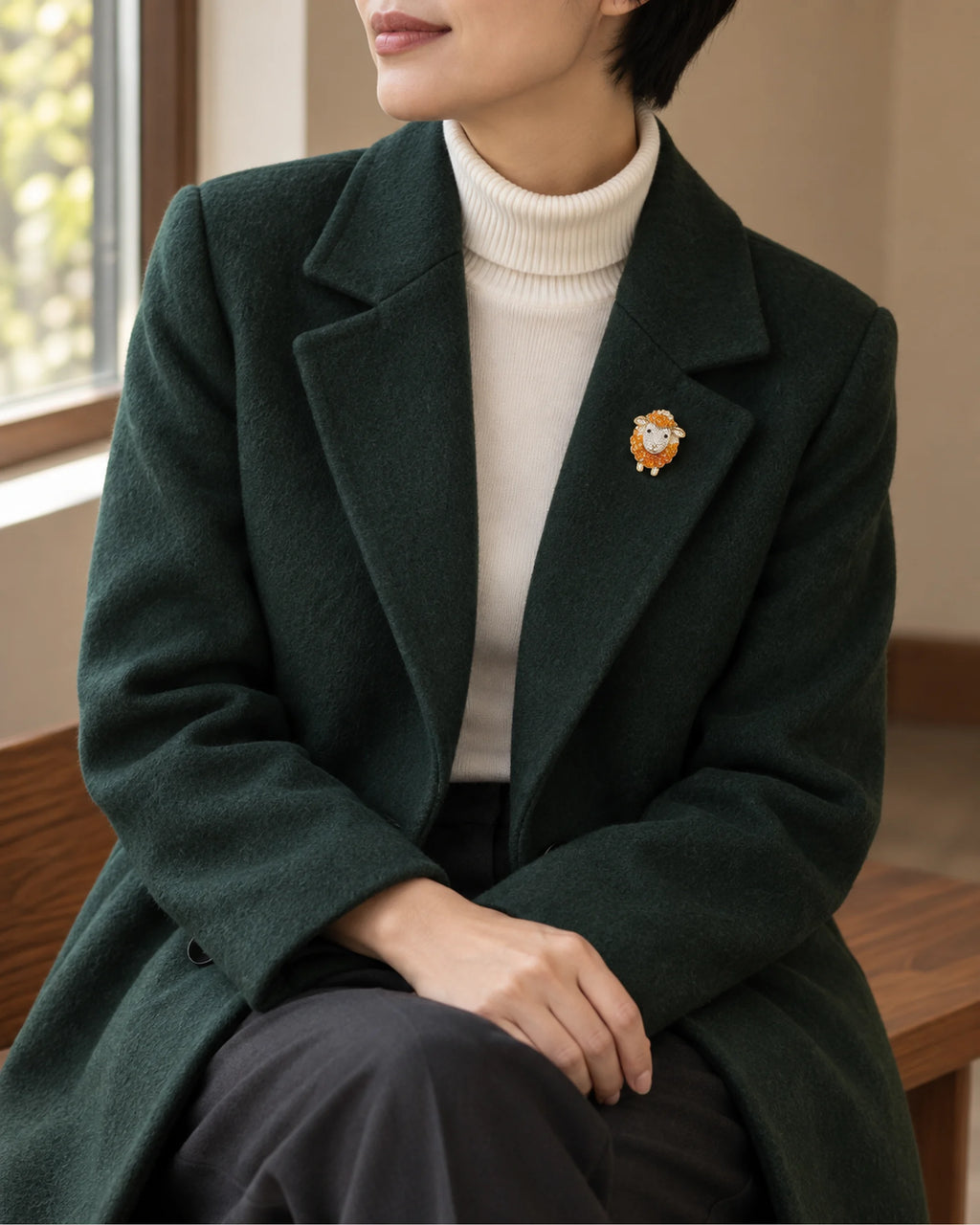 Small orange sheep brooch worn on a dark green coat, wider view