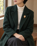 Small orange sheep brooch worn on a dark green coat, wider view