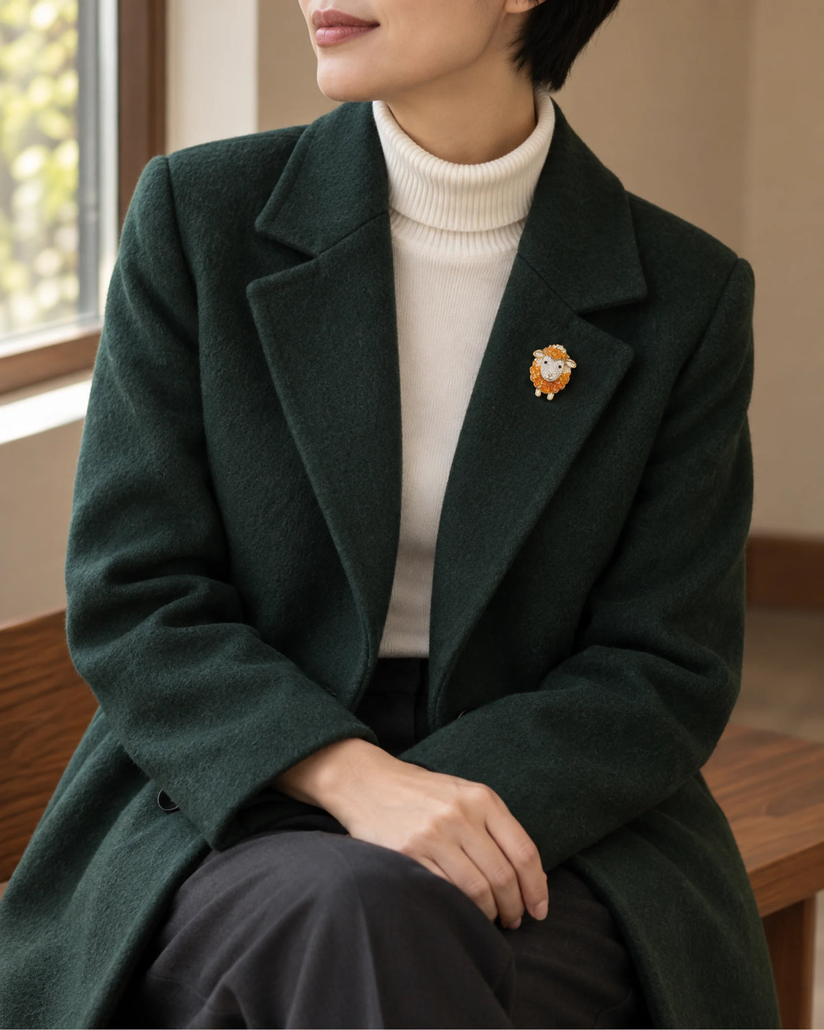 Small orange sheep brooch worn on a dark green coat, wider view