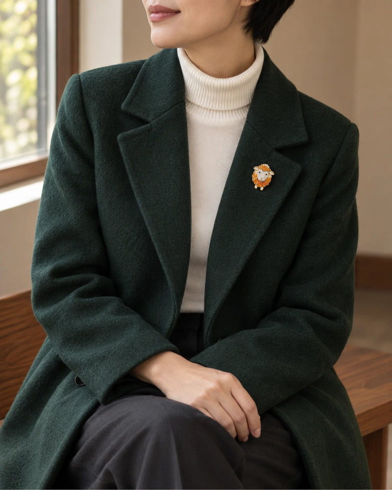 Small orange sheep brooch worn on a dark green coat, wider view