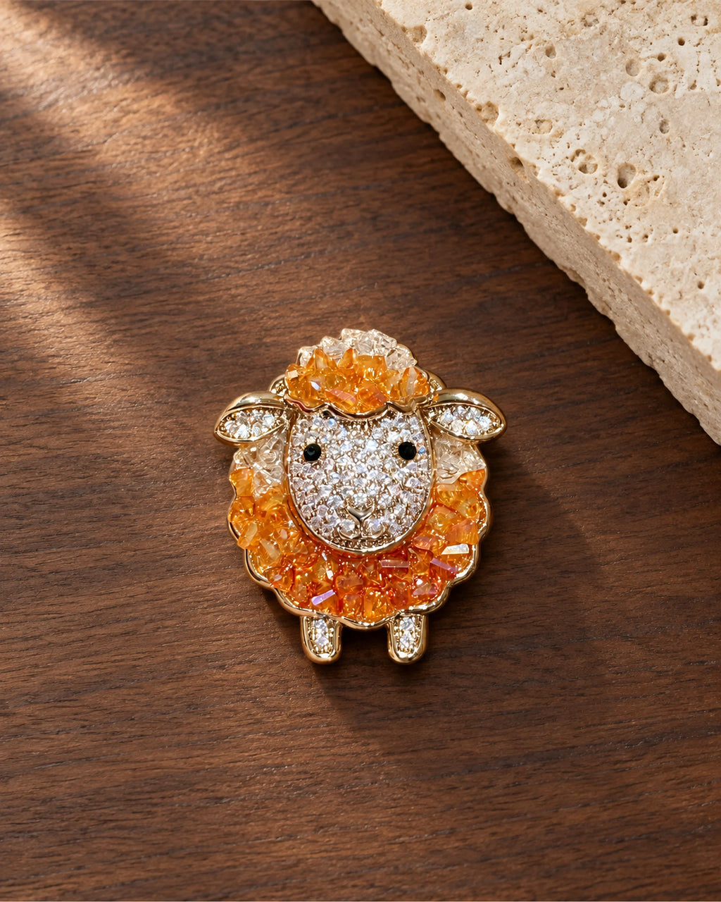 Mella Orange Crystal Sheep Brooch on walnut beside a pale stone slab