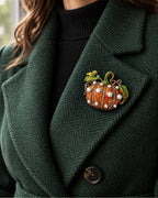 The Orange pumpkin rests inside a forest green coat lapel above a black knit.