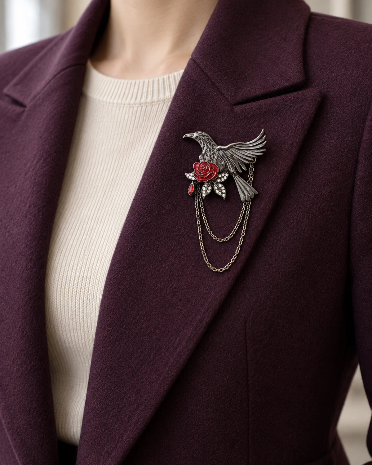 Noctra bird and rose chain brooch pinned within a plum blazer lapel