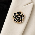 Noir black camellia brooch pinned inside an ivory folded blazer lapel in a local close view