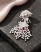 Noora parasol lady brooch resting on charcoal stone beside blush silk