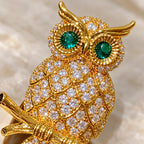 Green stone eyes and raised gold-plated feather borders surround the clear zircon.