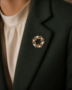 Close view of the Olea pearl wreath brooch pinned fully to a folded forest-green coat lapel at its true approximately 3.6 centimetre scale