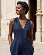 Pava turquoise-tone peacock pendant necklace worn with a navy dress in a wider sunlit courtyard portrait.