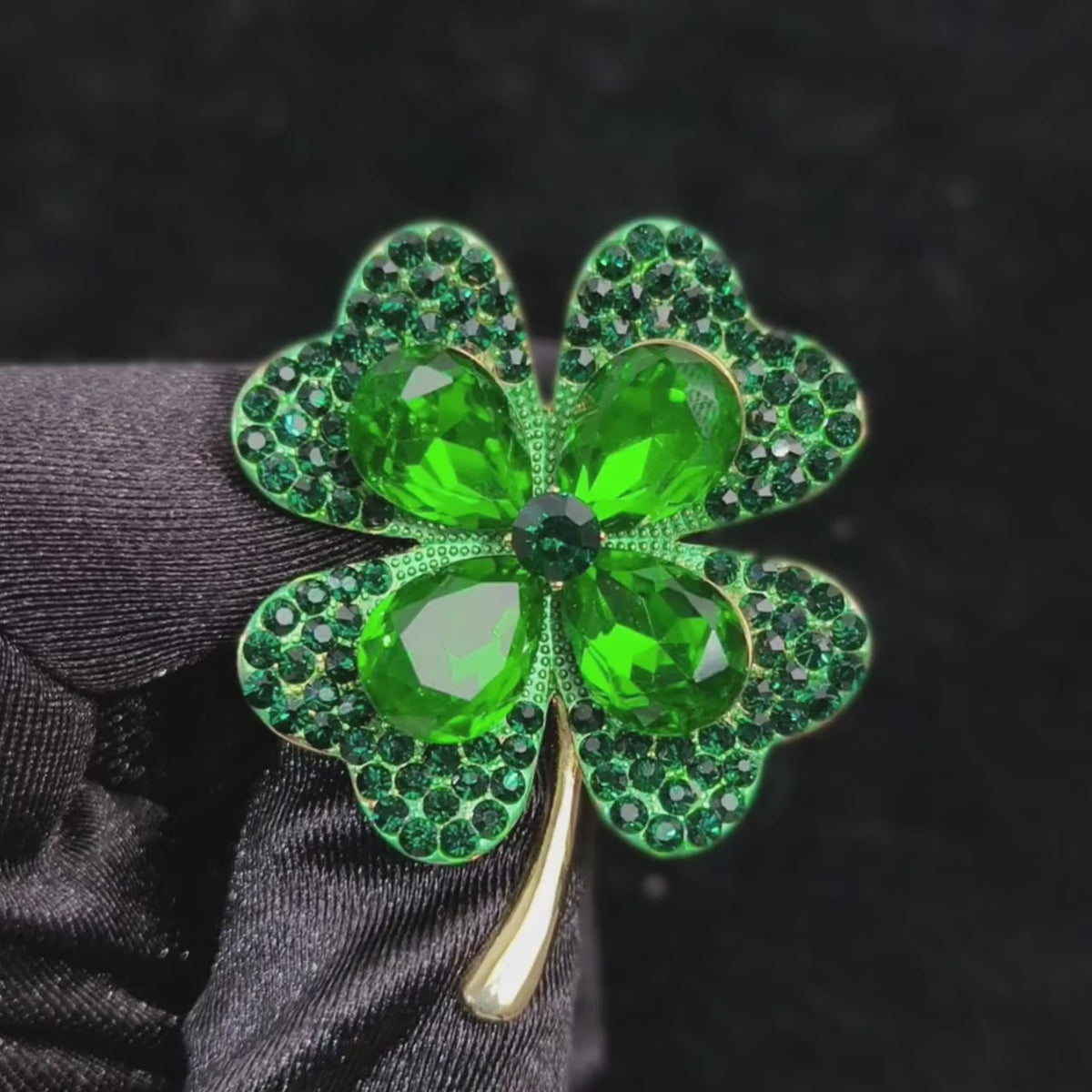 Toivo Green Crystal Clover Brooch held in a black glove as its layered green stones and gold-tone stem move in a square close-up.