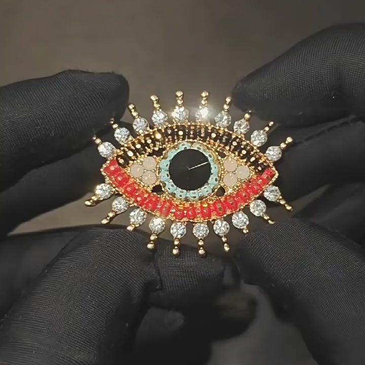 Suoja Multicolor Crystal Eye Brooch held in a black glove as its multicolour beadwork, clear accents and pin back move in a square close-up.