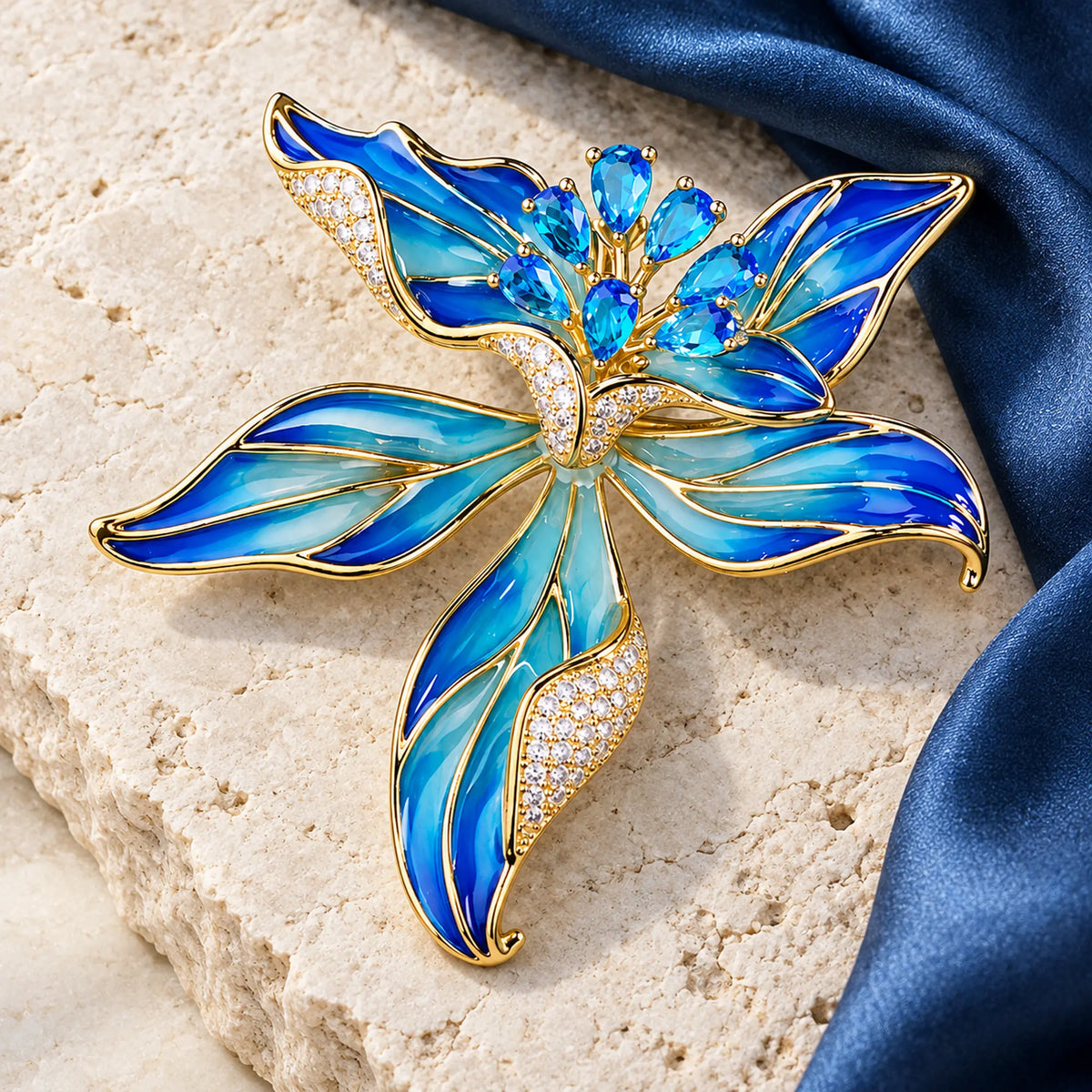 Complete Blue Riina brooch resting on pale limestone beside folded blue silk.