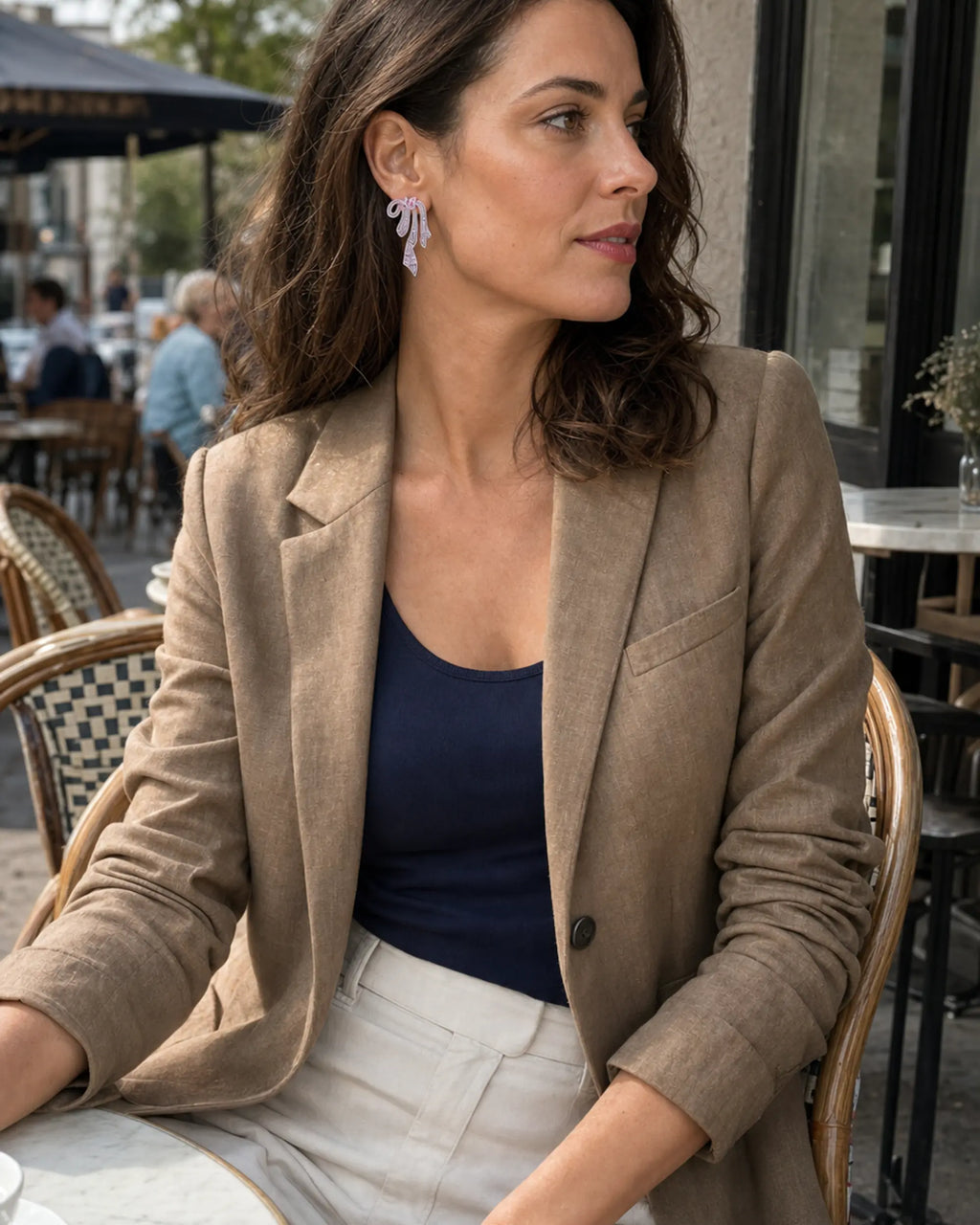 Woman wearing the Pink Runa Ribbon Bow Drop Earring with a tan blazer at an outdoor café