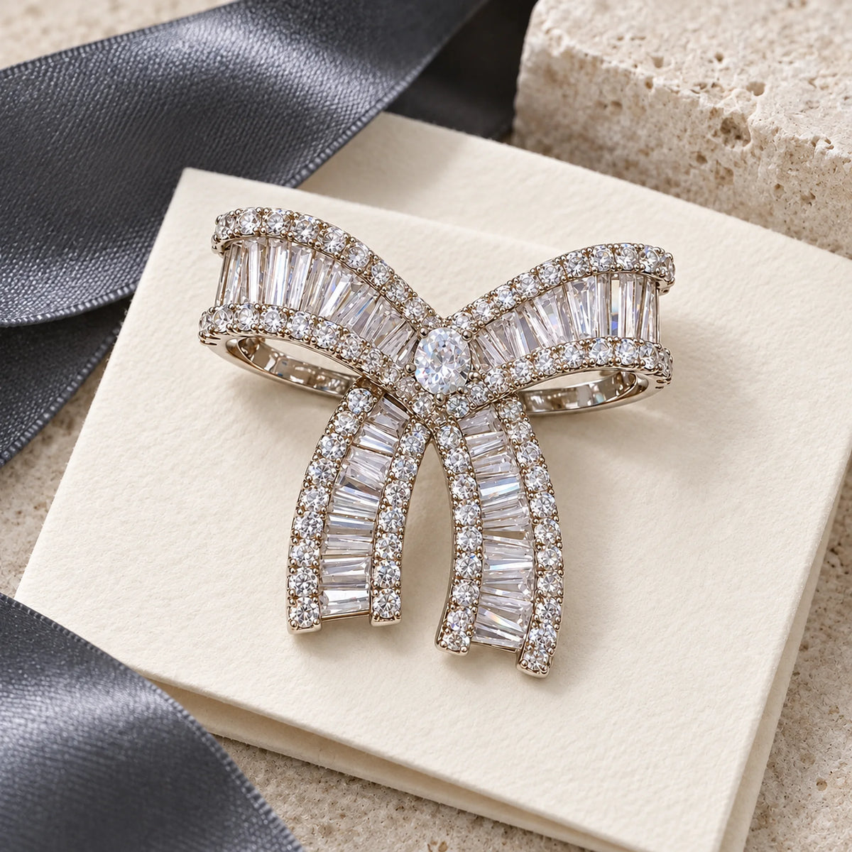 Complete Salla Baguette Zircon Bow Brooch resting on ivory paper beside silk and pale limestone.