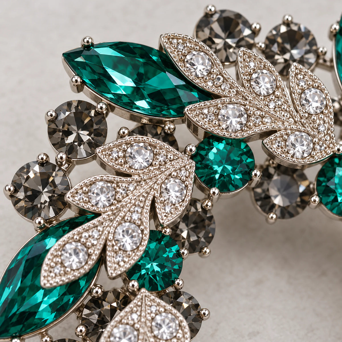 Close detail of clear pavé leaves, green faceted crystals and smoky-grey stones in the brooch setting
