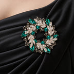 Green crystal leaf wreath brooch pinned to gathered black satin evening-dress fabric