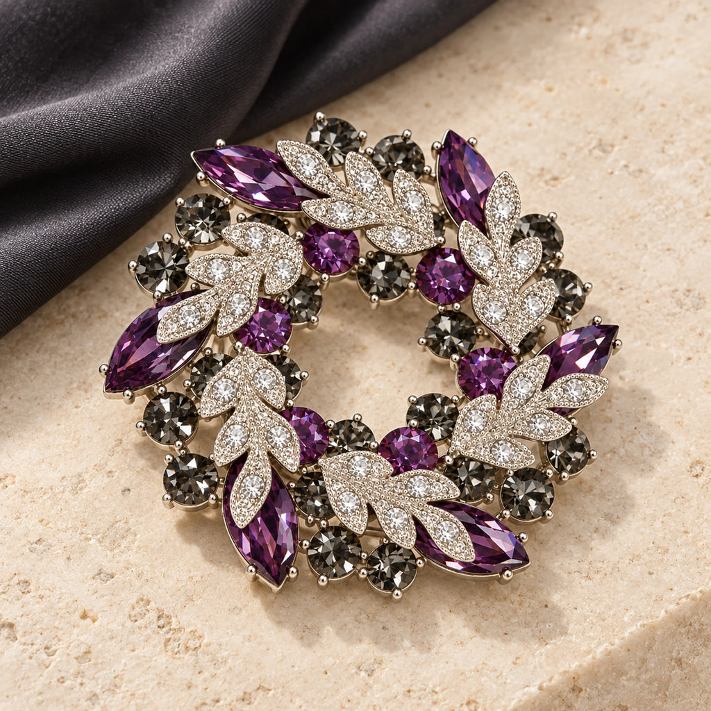Purple crystal leaf wreath brooch resting on pale limestone beside charcoal fabric