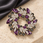 Purple crystal leaf wreath brooch resting on pale limestone beside charcoal fabric