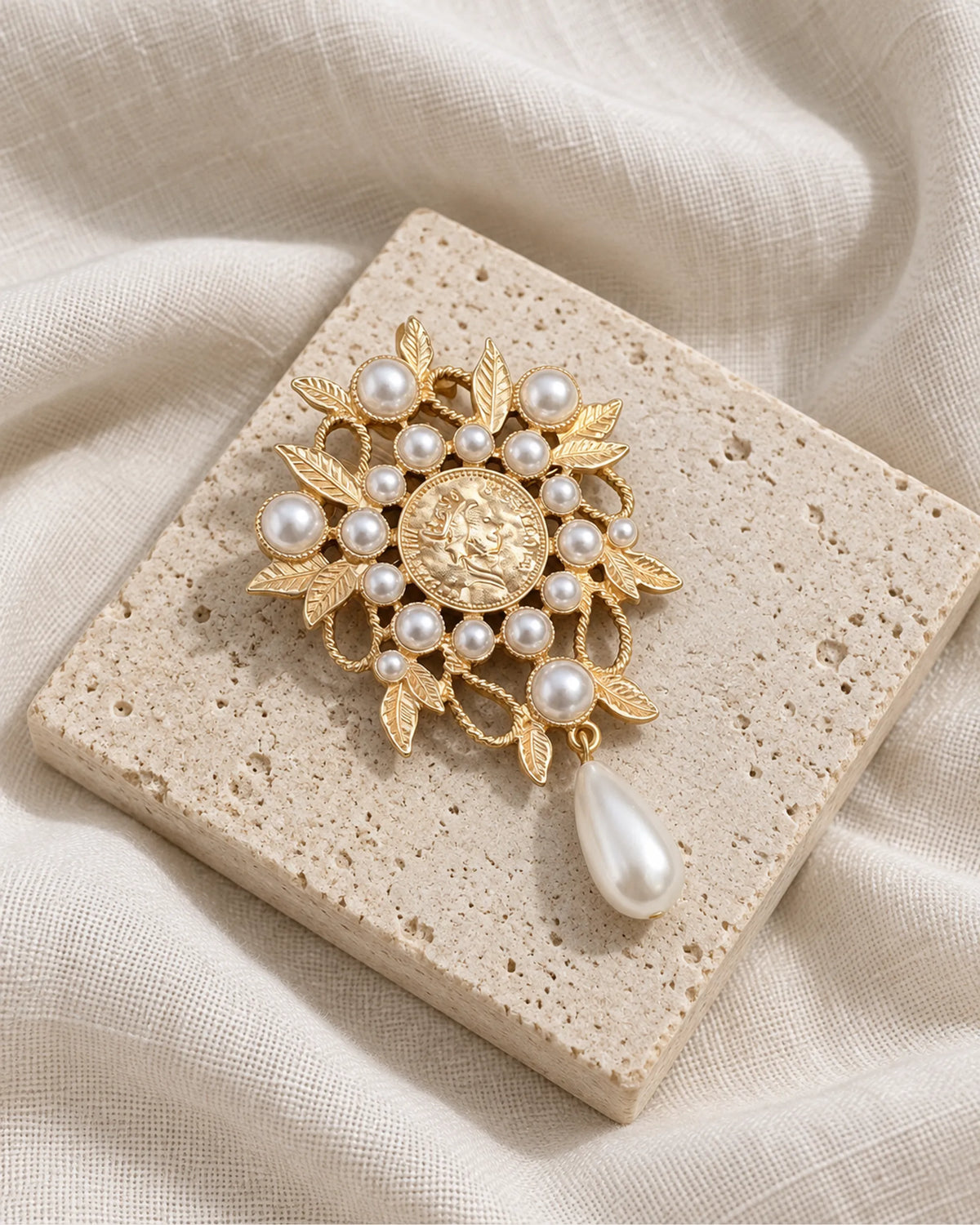 Signe Coin Medallion Drop Brooch — front view on a stone tile and ivory linen