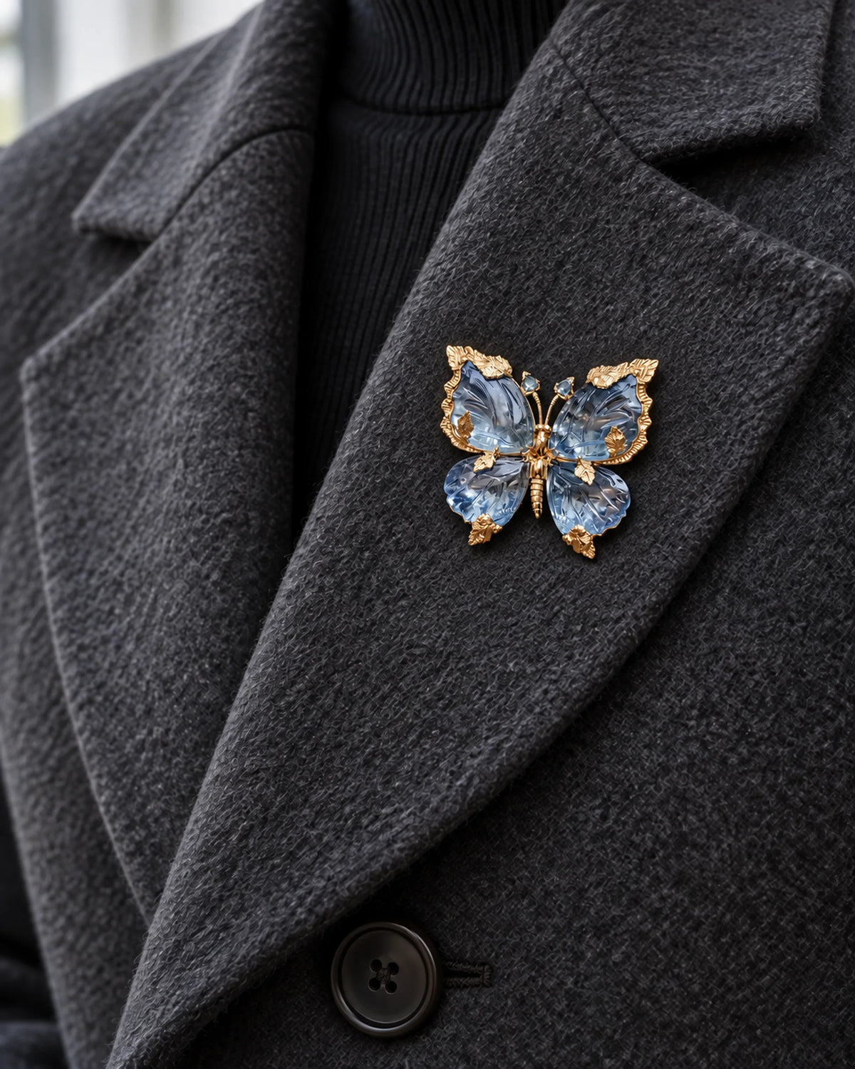 Sini sculpted blue crystal butterfly brooch pinned within a charcoal wool coat lapel.