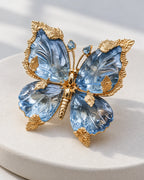 Sini blue crystal butterfly brooch in an angled front view on a pale ceramic display.