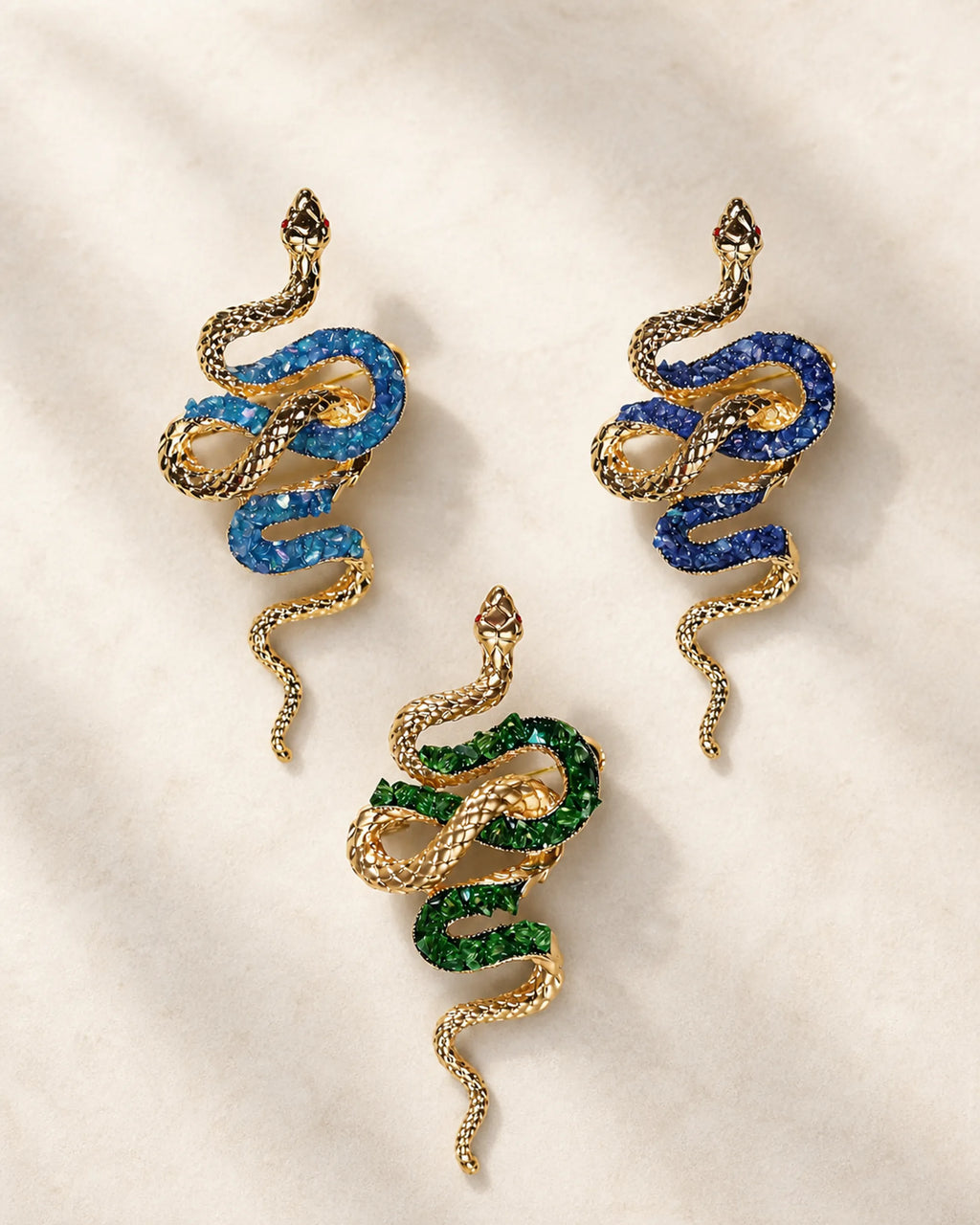Three Sisu snake brooch variants in lake blue, royal blue and green shown together at equal scale