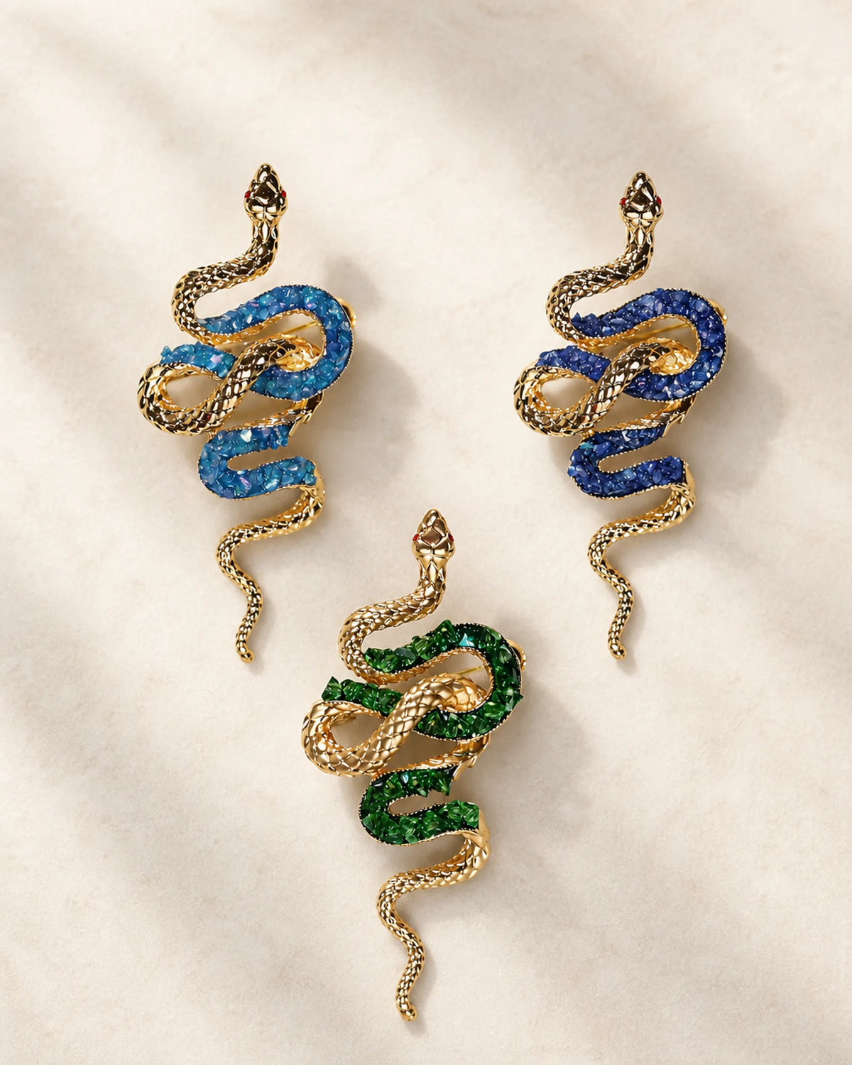 Three Sisu snake brooch variants in lake blue, royal blue and green shown together at equal scale