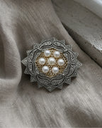 Silver-tone pearl rosette brooch resting on folded linen beside pale stone.