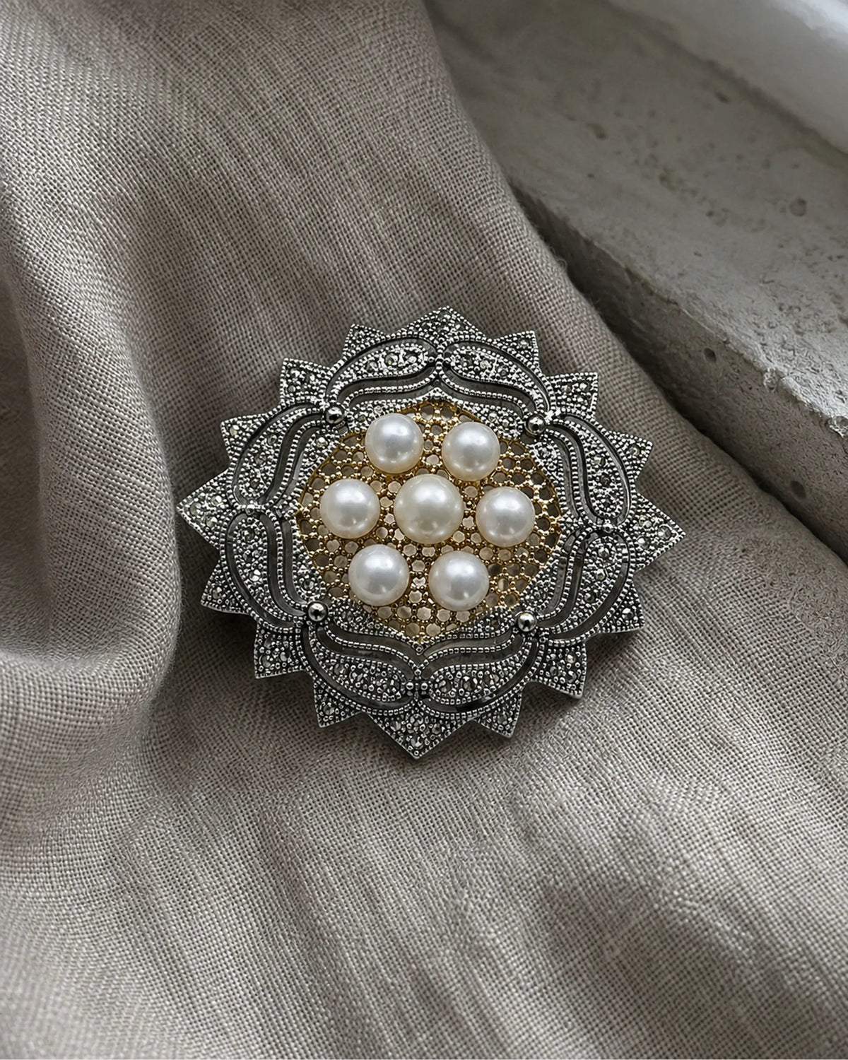 Silver-tone pearl rosette brooch resting on folded linen beside pale stone.