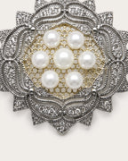 Close view of seven freshwater pearls and the rosette brooch’s pierced center and silver-tone scrollwork.