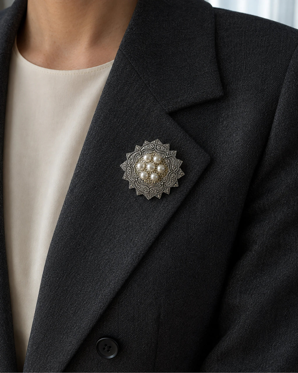Seven-pearl rosette brooch pinned within the broad folded lapel of a charcoal blazer.
