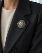 Seven-pearl rosette brooch pinned within the broad folded lapel of a charcoal blazer.