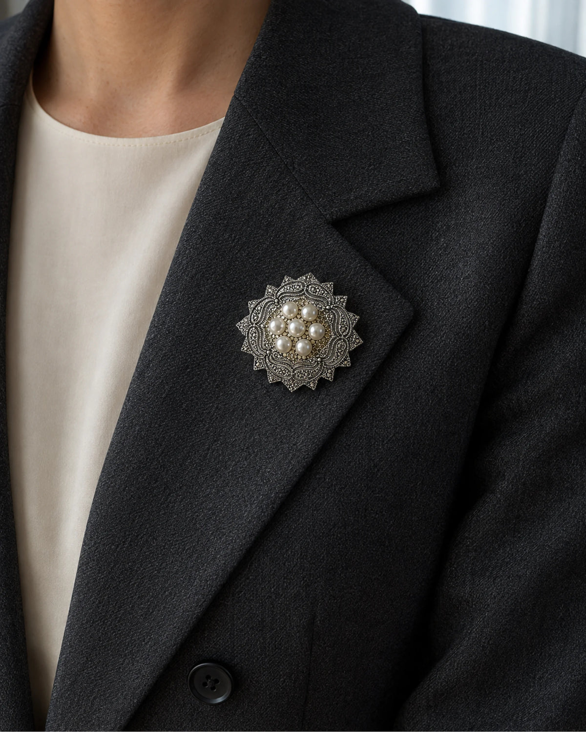 Seven-pearl rosette brooch pinned within the broad folded lapel of a charcoal blazer.