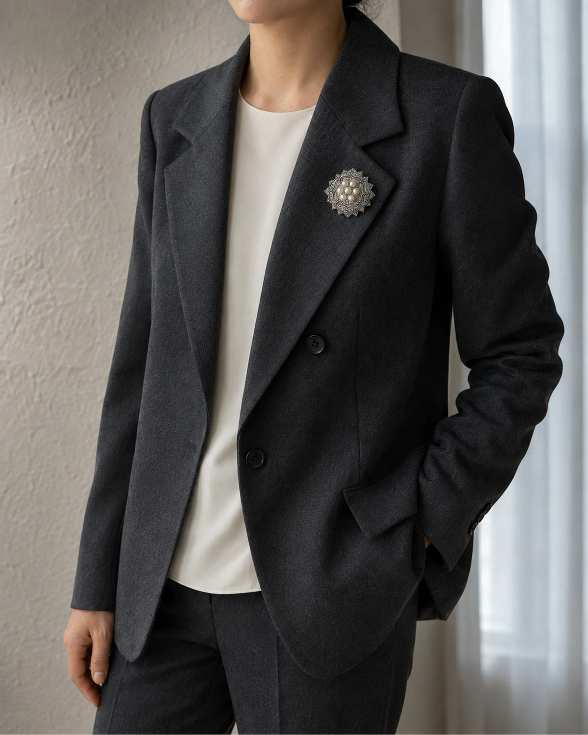 Wider outfit view of Solveig pearl rosette brooch on a charcoal blazer over an ivory top.