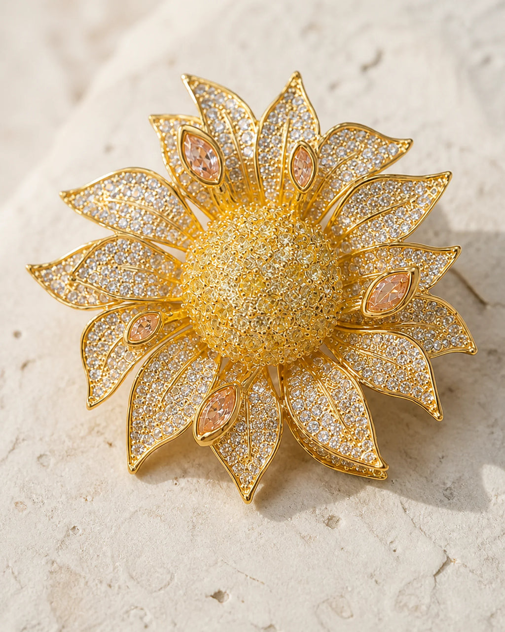 Macro view of the layered gold-tone petals, clear crystals and peach marquise accents of the Solvi Sunflower Brooch