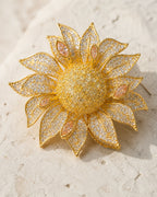 Macro view of the layered gold-tone petals, clear crystals and peach marquise accents of the Solvi Sunflower Brooch