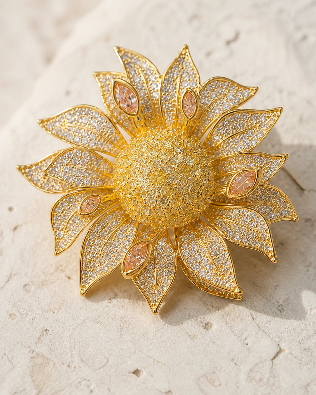 Macro view of the layered gold-tone petals, clear crystals and peach marquise accents of the Solvi Sunflower Brooch