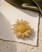 Solvi Sunflower Brooch resting on pale travertine, ivory paper and olive silk in an original TUUGLOW still life