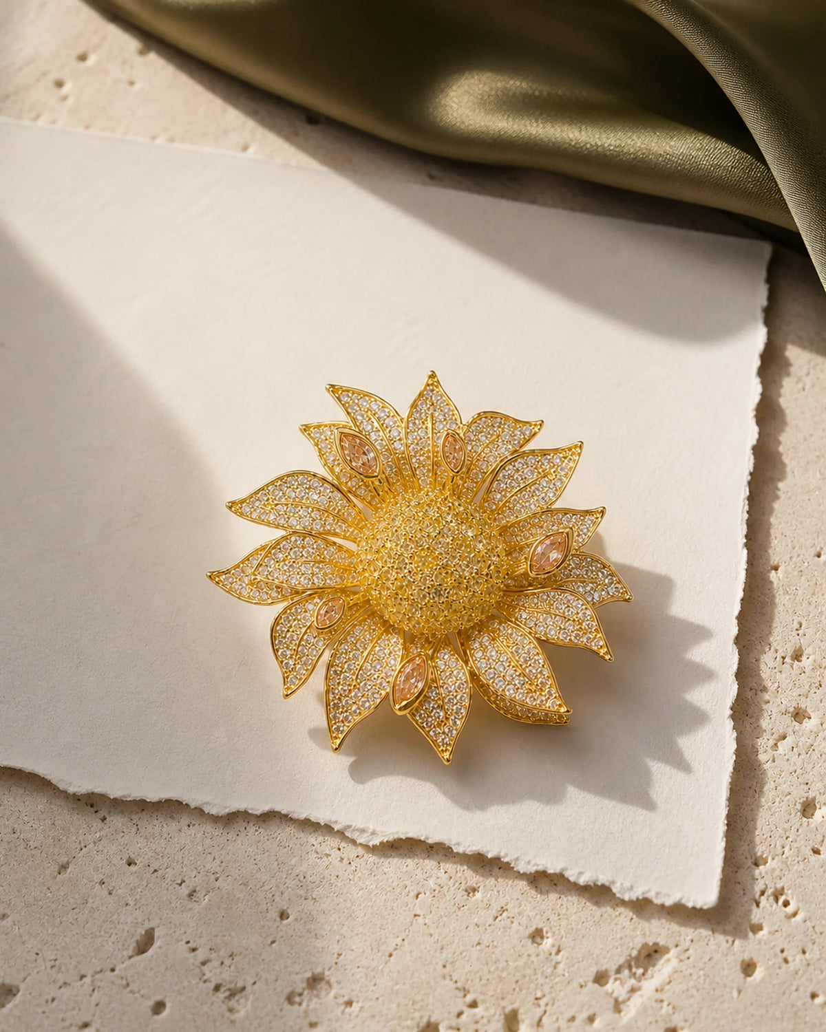 Solvi Sunflower Brooch resting on pale travertine, ivory paper and olive silk in an original TUUGLOW still life