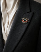 Close view of the Suoja eye brooch pinned fully to a folded charcoal blazer lapel at its true approximately 4.0 by 3.2 centimetre scale