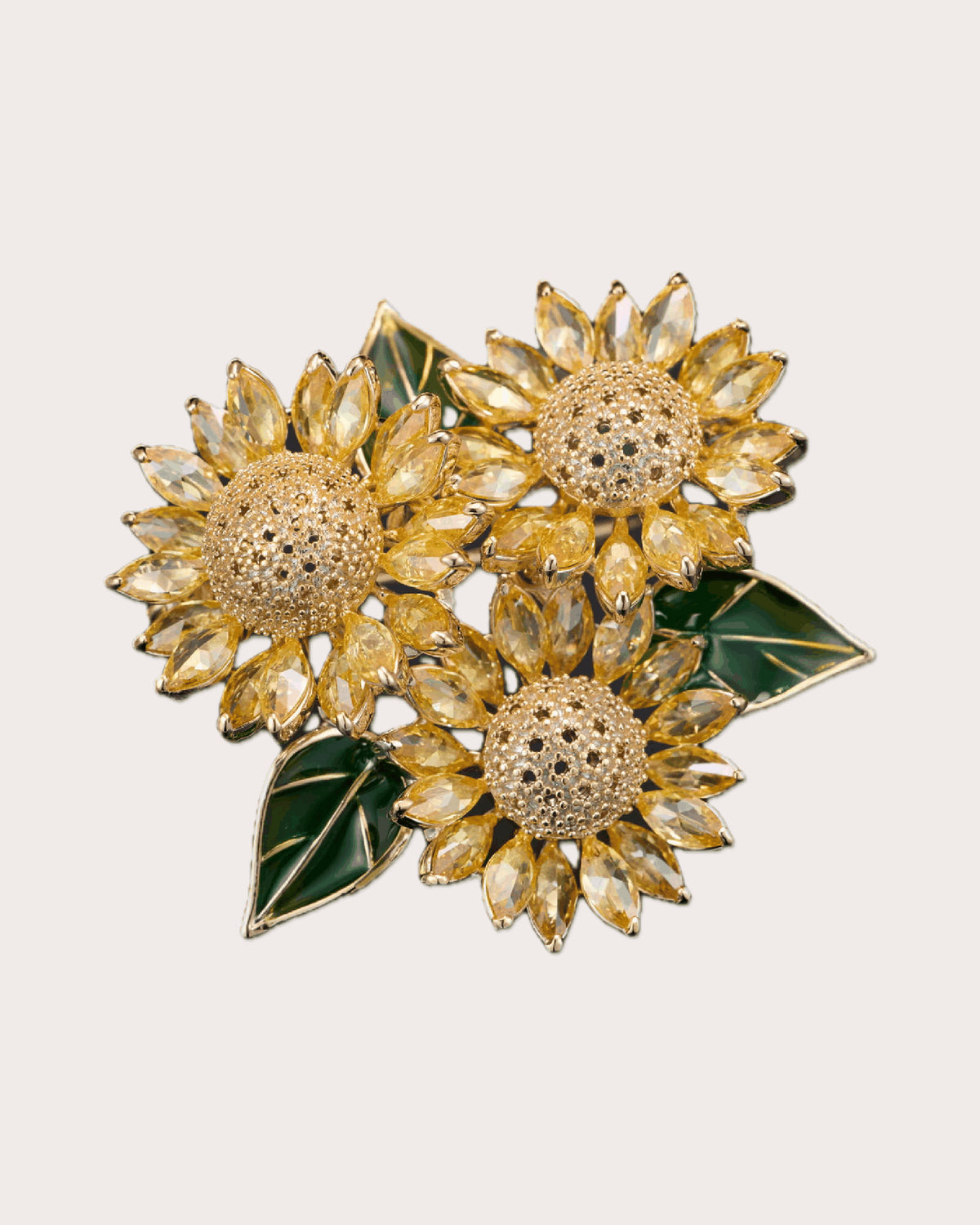Suvia yellow crystal sunflower trio brooch with gold-tone centers and green leaves on a warm neutral background