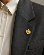 Close view of the 2.2 cm Taimi Mini Gold Camellia Brooch pinned to the folded lapel of a charcoal blazer